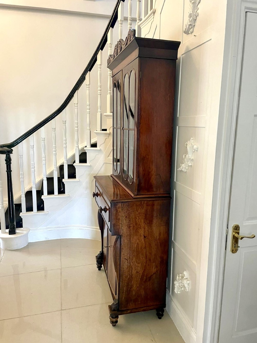 An antique Regency mahogany secretaire bookcase featuring a carved scroll pediment, glazed upper doors, a fall-front desk drawer, and a lower two-door cupboard. View XII