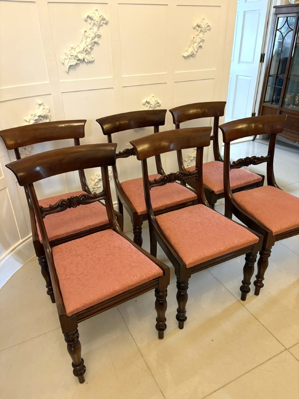 Set of six antique William IV mahogany dining chairs with curved crest rails, scroll carved crossbars, turned front legs, and pink damask upholstered drop-in seats. View X