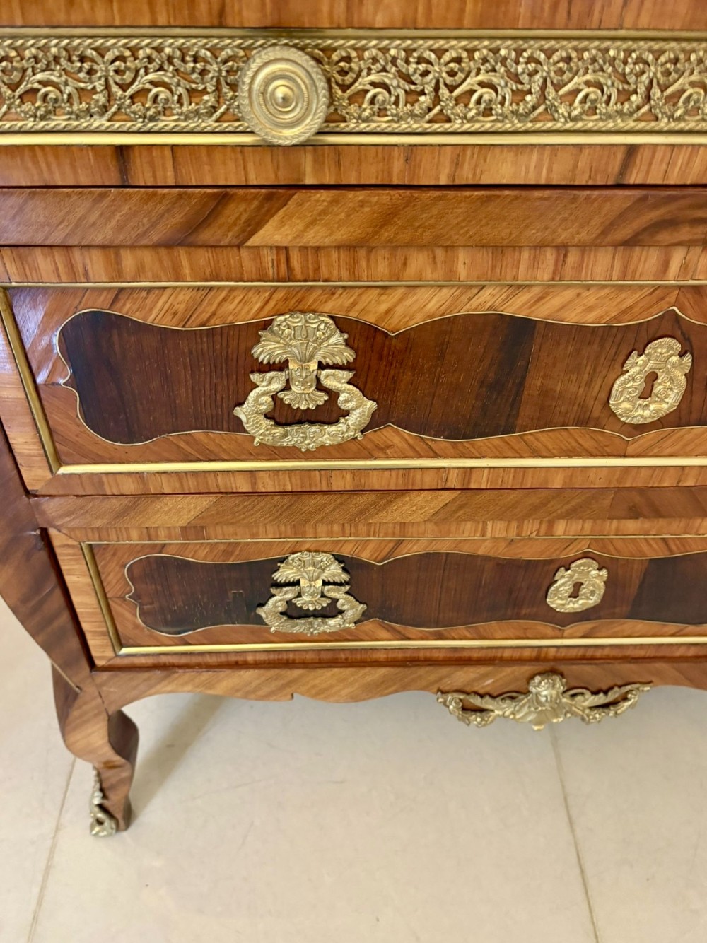 An antique French style commode chest featuring a dark grey veined marble top, decorative walnut veneers, cast brass mounts, and cabriole legs. View VI
