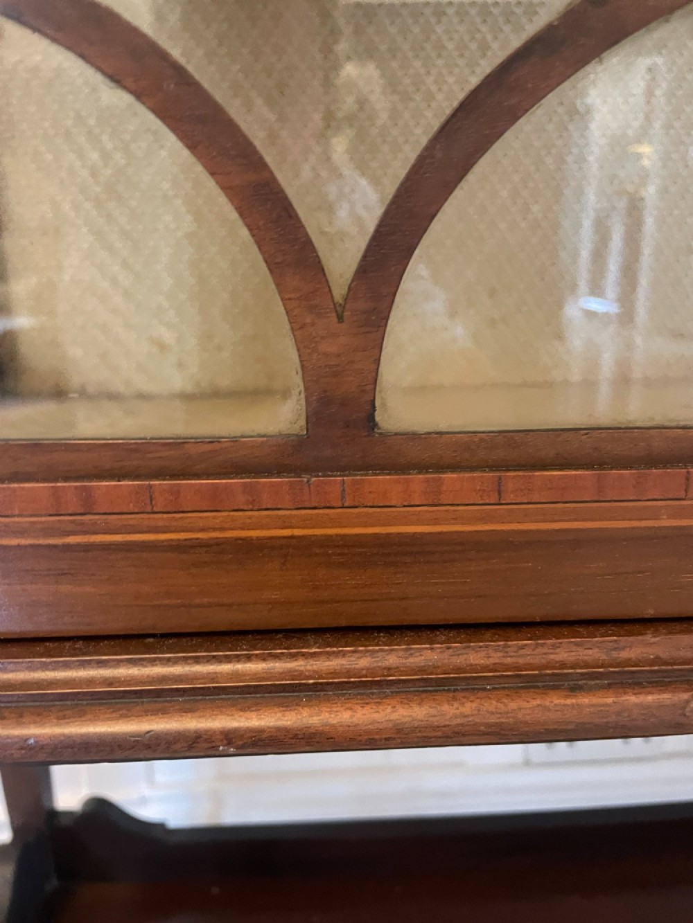 An Edwardian mahogany display cabinet featuring glazed doors with astragal bars, a central marquetry inlay medallion, tapering square legs, and an undertier shelf. View III