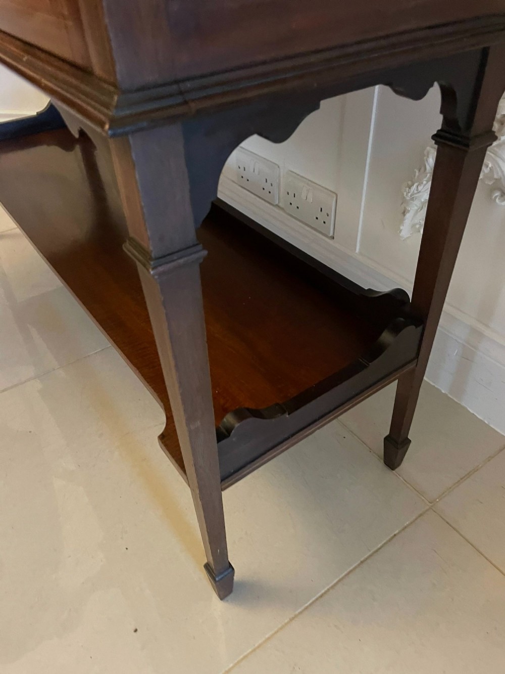 An Edwardian mahogany display cabinet featuring glazed doors with astragal bars, a central marquetry inlay medallion, tapering square legs, and an undertier shelf. View VII