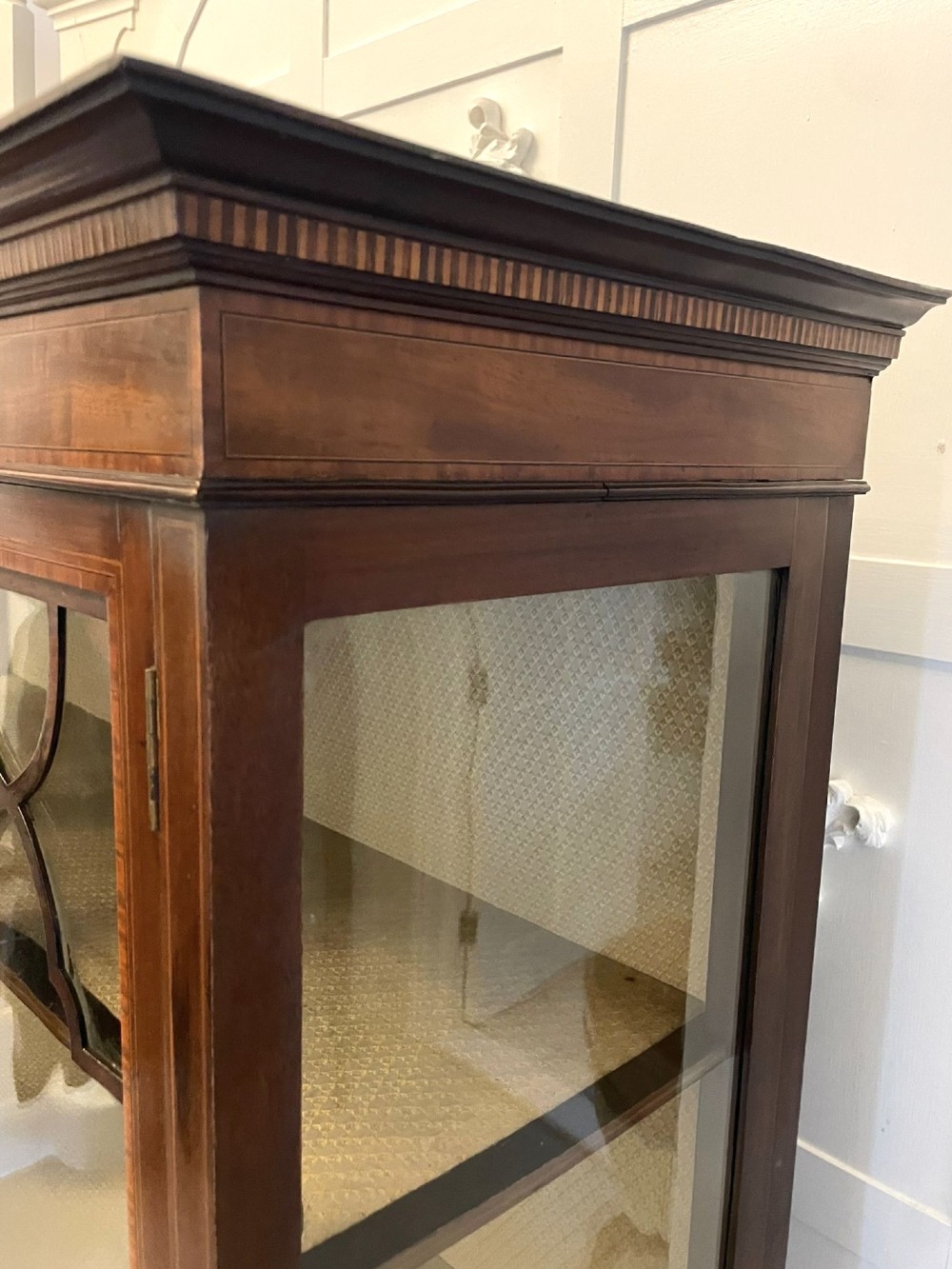 An Edwardian mahogany display cabinet featuring glazed doors with astragal bars, a central marquetry inlay medallion, tapering square legs, and an undertier shelf. View VIII