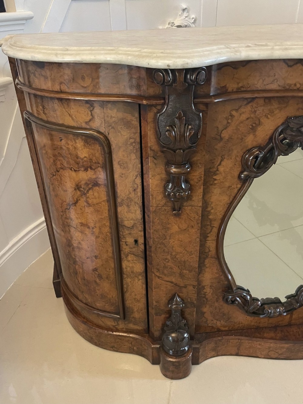 A Victorian burr walnut credenza featuring a serpentine white marble top above two central oval mirrored doors and carved scroll accents. View II