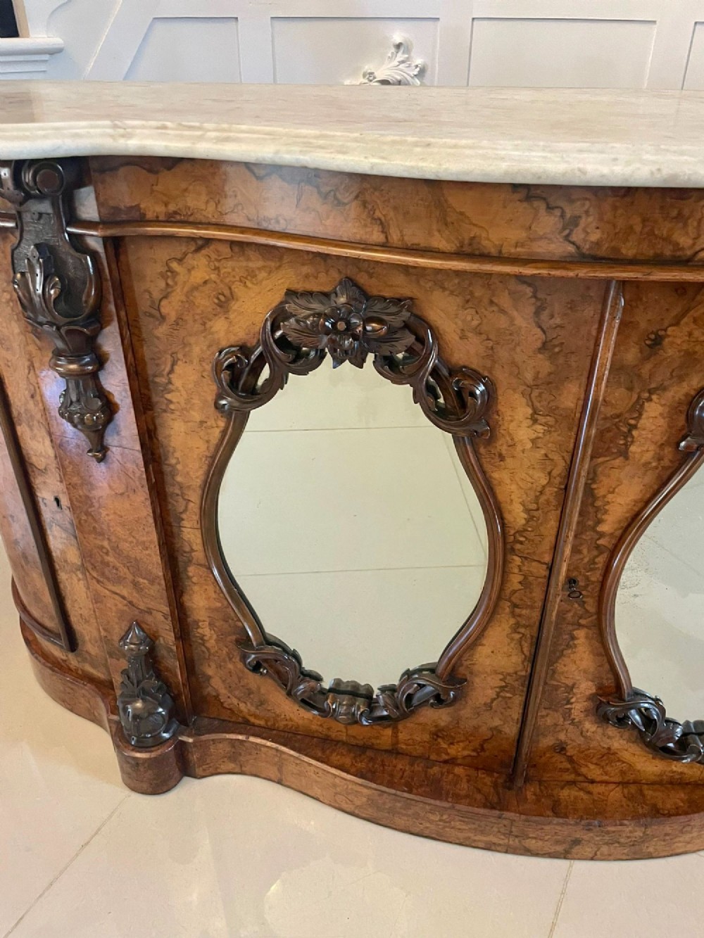A Victorian burr walnut credenza featuring a serpentine white marble top above two central oval mirrored doors and carved scroll accents. View V