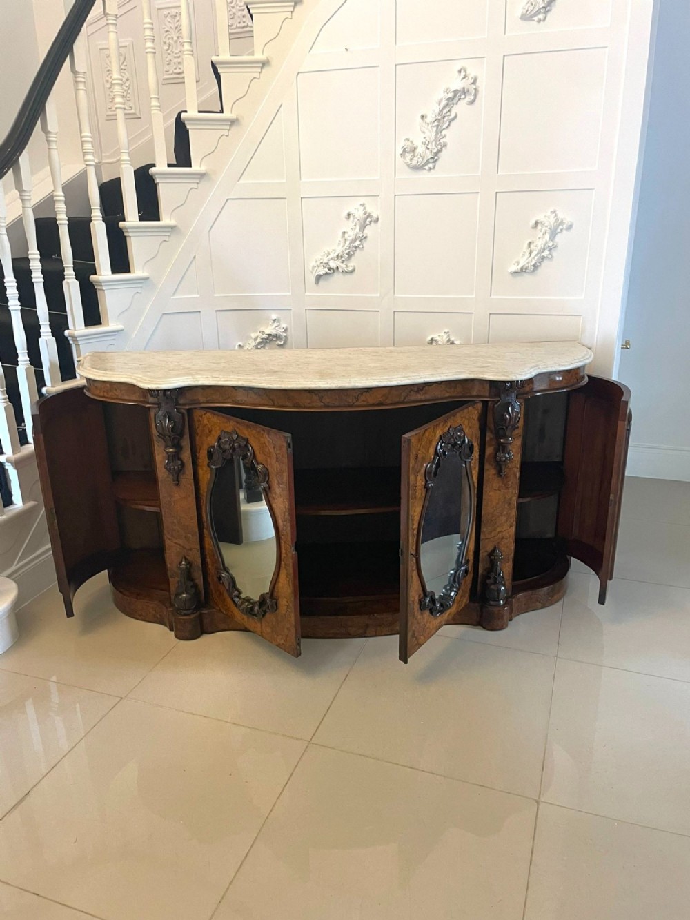 A Victorian burr walnut credenza featuring a serpentine white marble top above two central oval mirrored doors and carved scroll accents. View VI