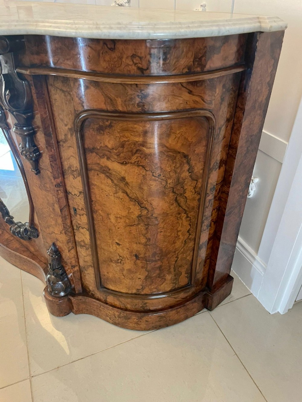 A Victorian burr walnut credenza featuring a serpentine white marble top above two central oval mirrored doors and carved scroll accents. View VII