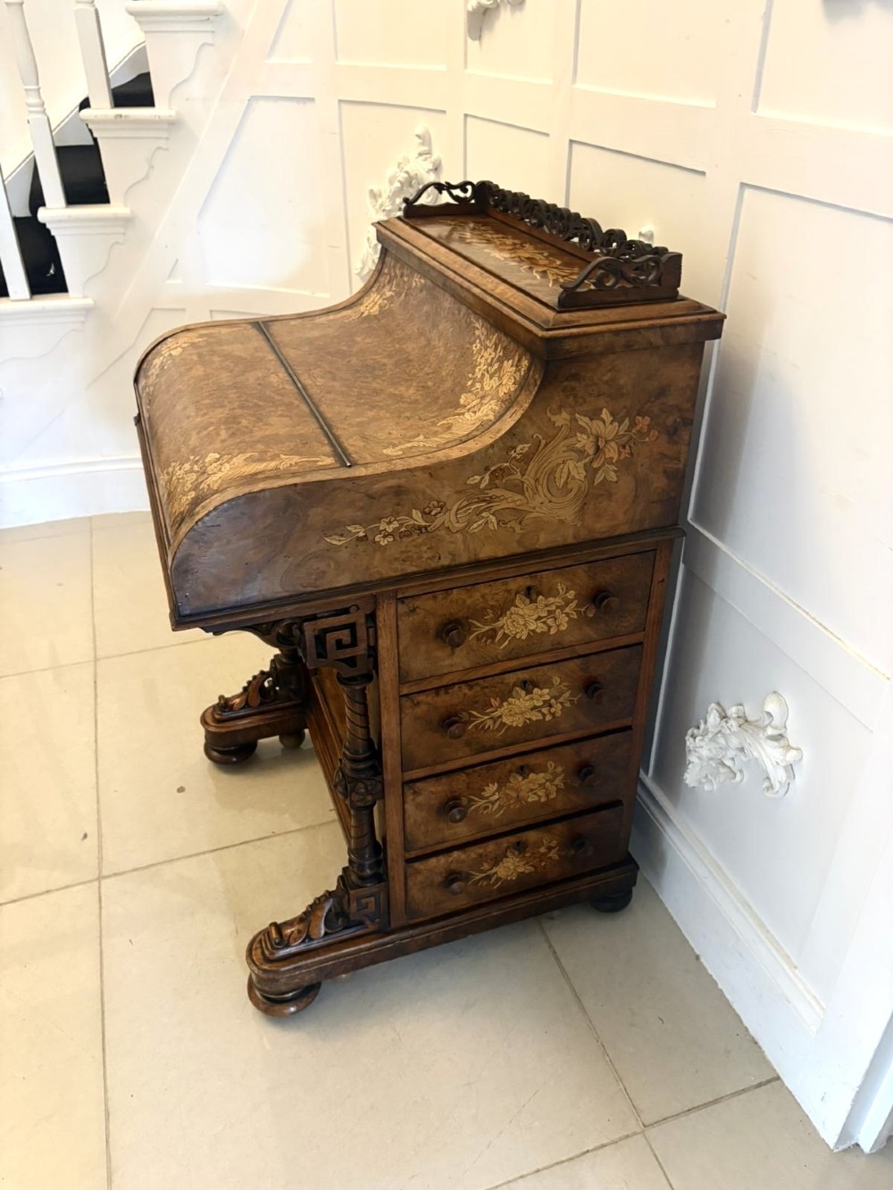 A Victorian burr walnut piano top davenport desk featuring floral marquetry, side drawers with turned wooden knobs, and carved supports.