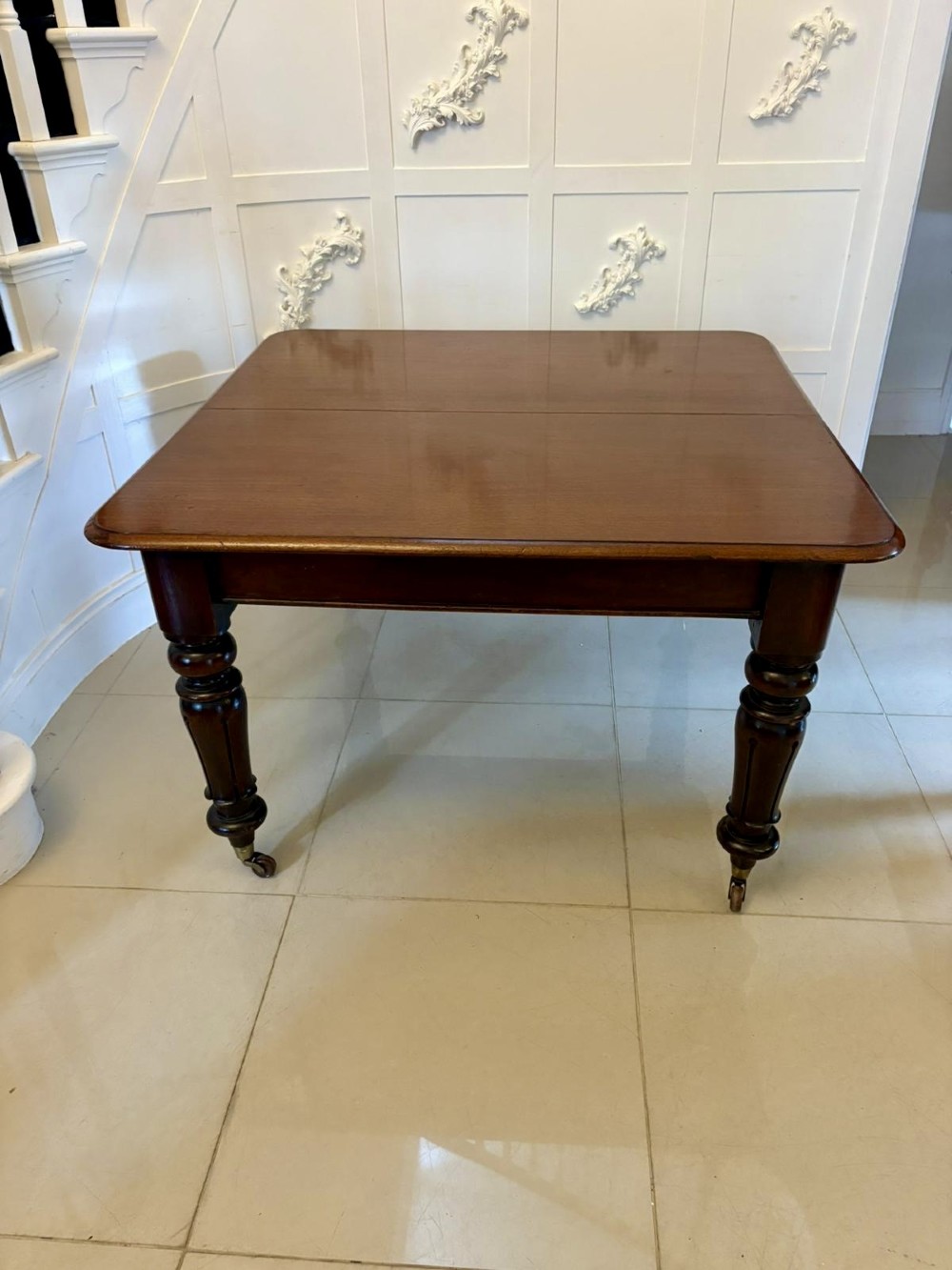 A large Victorian extending mahogany dining table featuring rounded corners, turned legs, brass castors, and a polished dark wood surface. View III