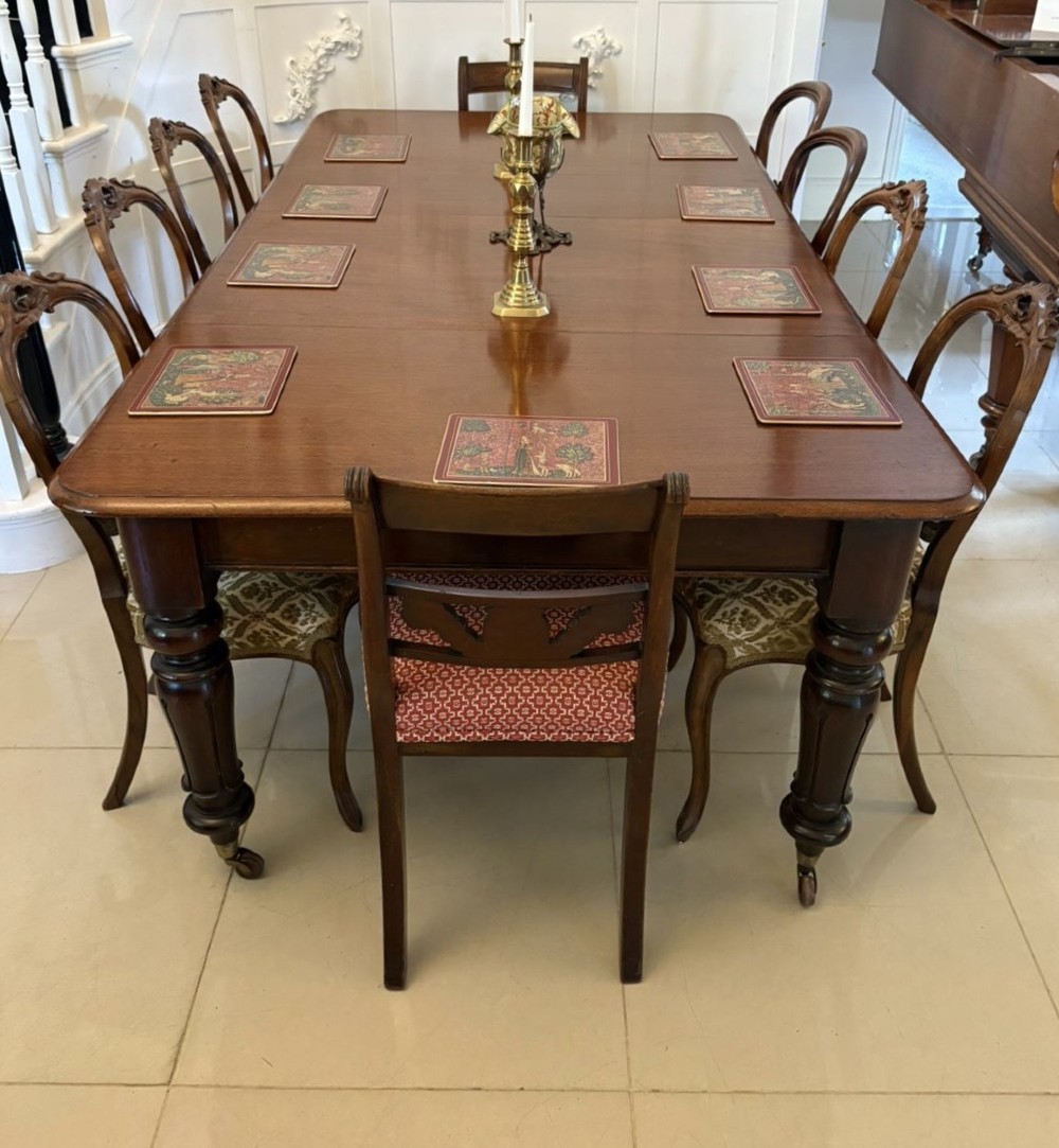 A large Victorian extending mahogany dining table featuring rounded corners, turned legs, brass castors, and a polished dark wood surface. View VIII