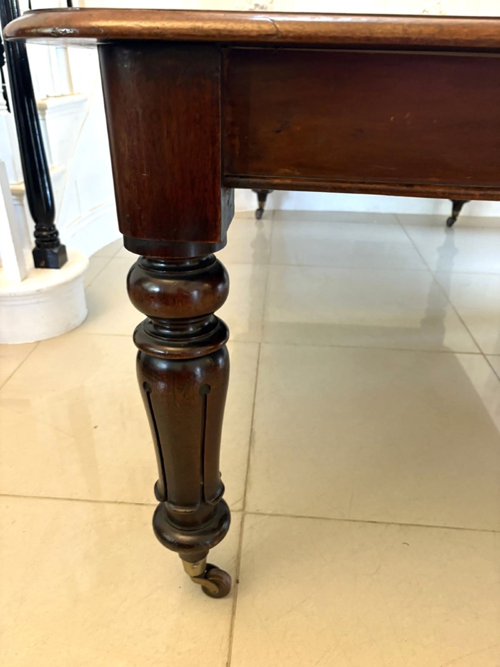 A large Victorian extending mahogany dining table featuring rounded corners, turned legs, brass castors, and a polished dark wood surface. View X