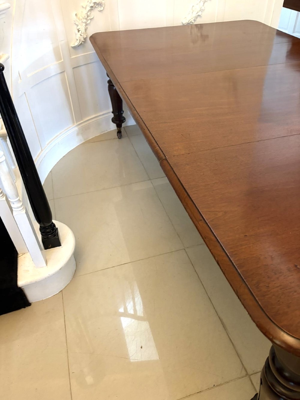 A large Victorian extending mahogany dining table featuring rounded corners, turned legs, brass castors, and a polished dark wood surface. View XI