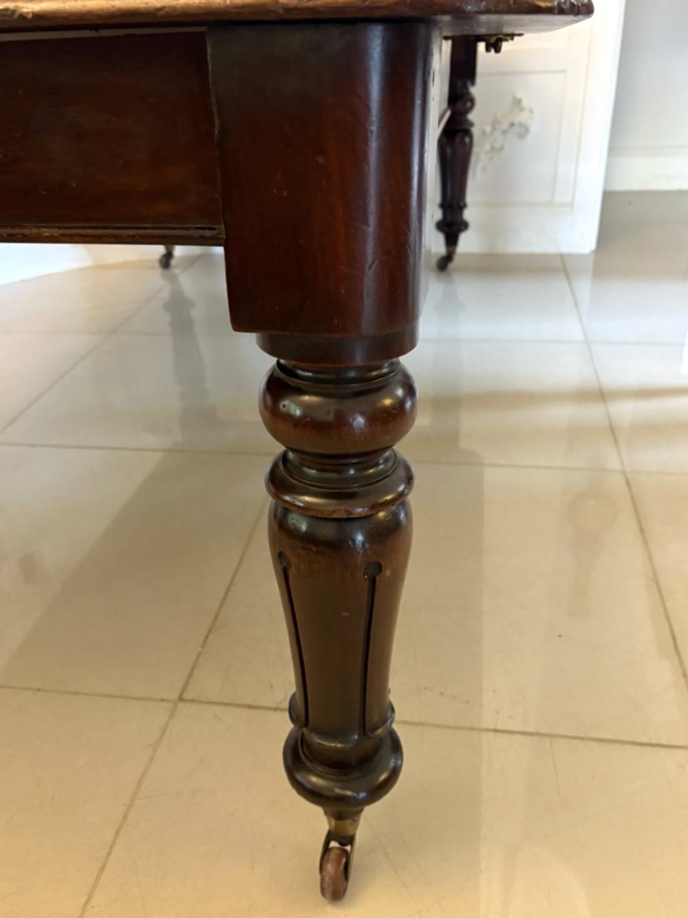 A large Victorian extending mahogany dining table featuring rounded corners, turned legs, brass castors, and a polished dark wood surface. View XII
