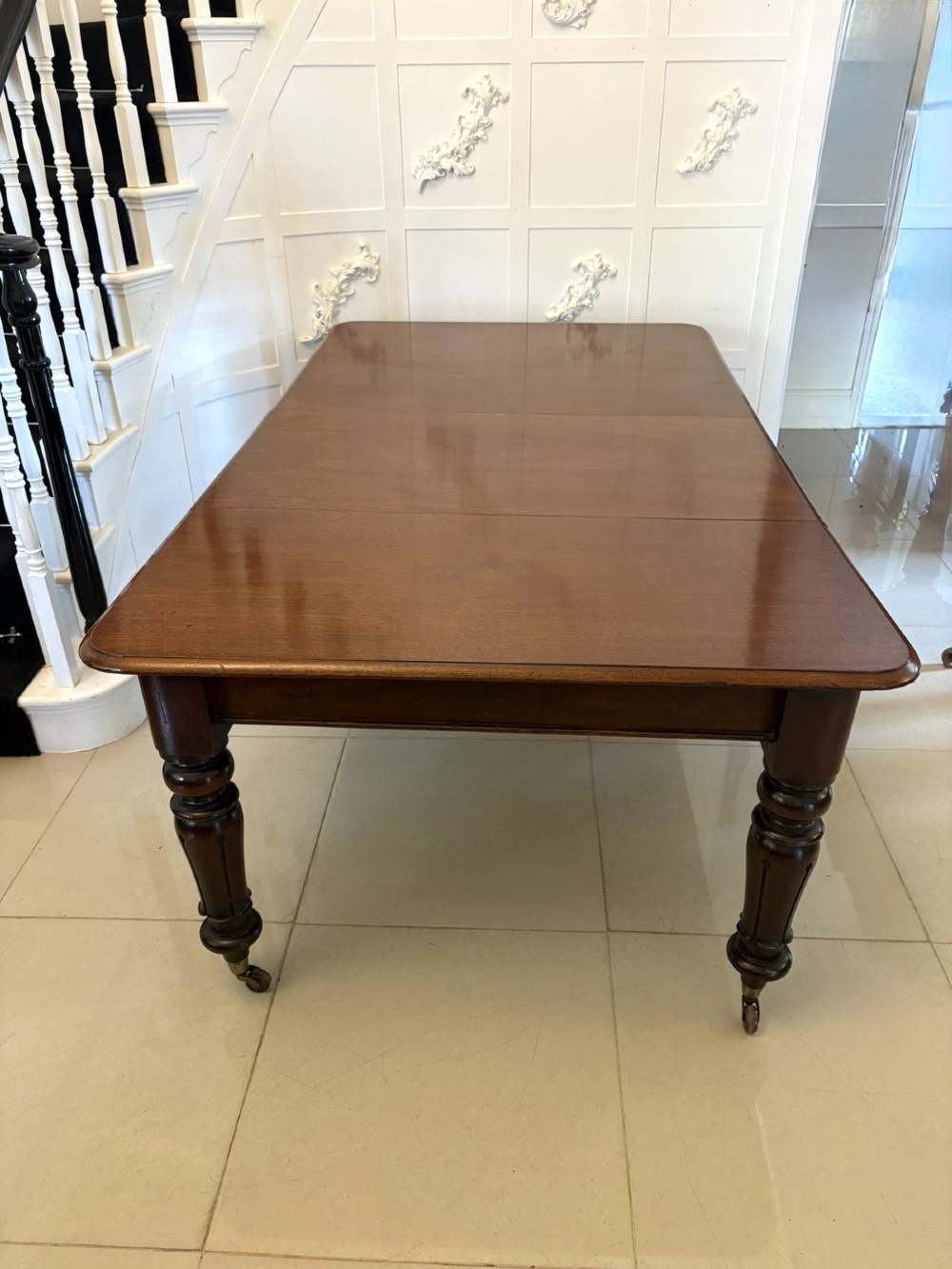 A large Victorian extending mahogany dining table featuring rounded corners, turned legs, brass castors, and a polished dark wood surface.