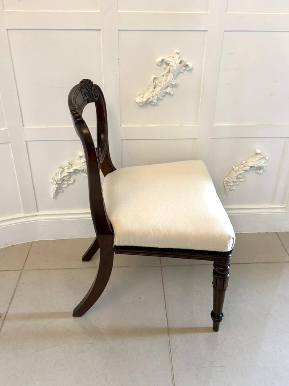 A set of ten antique English Regency mahogany dining chairs with carved balloon backs, cream upholstered seats, and turned front legs. View V