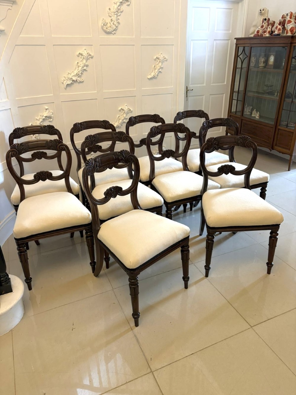 A set of ten antique English Regency mahogany dining chairs with carved balloon backs, cream upholstered seats, and turned front legs. View VIII