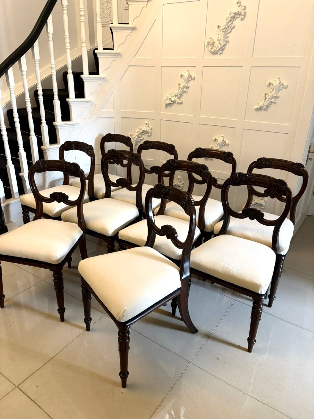 A set of ten antique English Regency mahogany dining chairs with carved balloon backs, cream upholstered seats, and turned front legs. View IX
