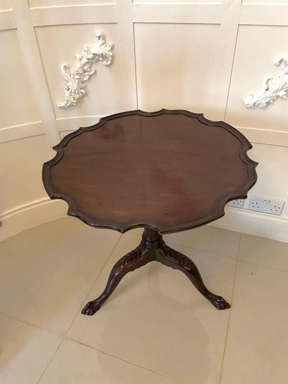 An antique George III mahogany tilt-top table featuring a scalloped pie-crust rim supported by a carved central pedestal and tripod cabriole legs. View IV