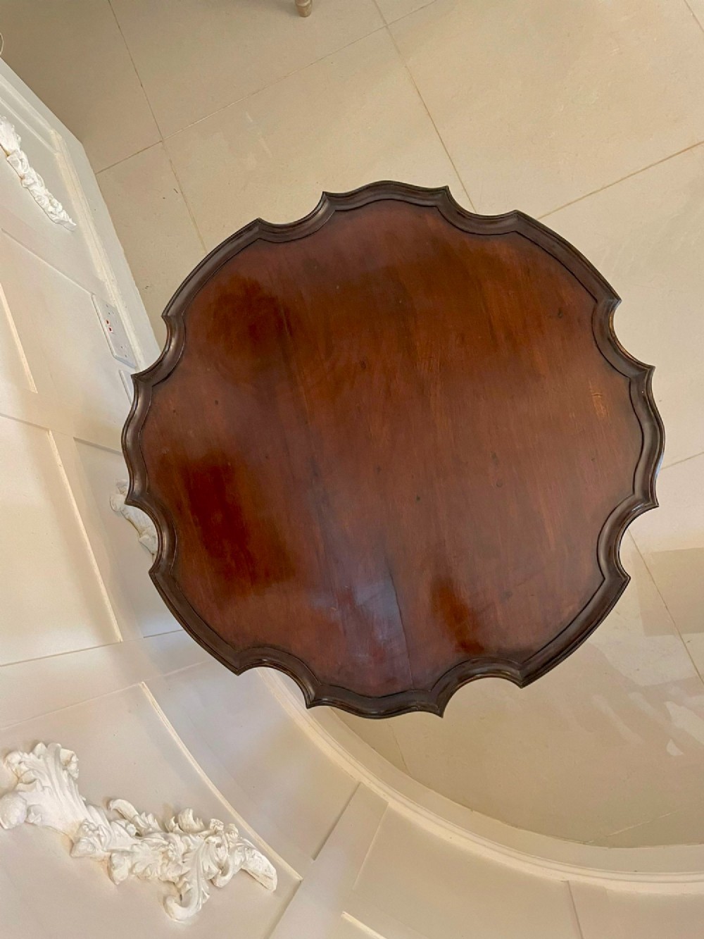An antique George III mahogany tilt-top table featuring a scalloped pie-crust rim supported by a carved central pedestal and tripod cabriole legs. View V