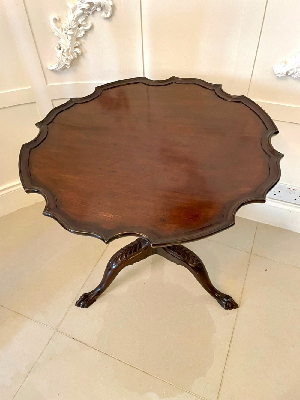An antique George III mahogany tilt-top table featuring a scalloped pie-crust rim supported by a carved central pedestal and tripod cabriole legs. View VI