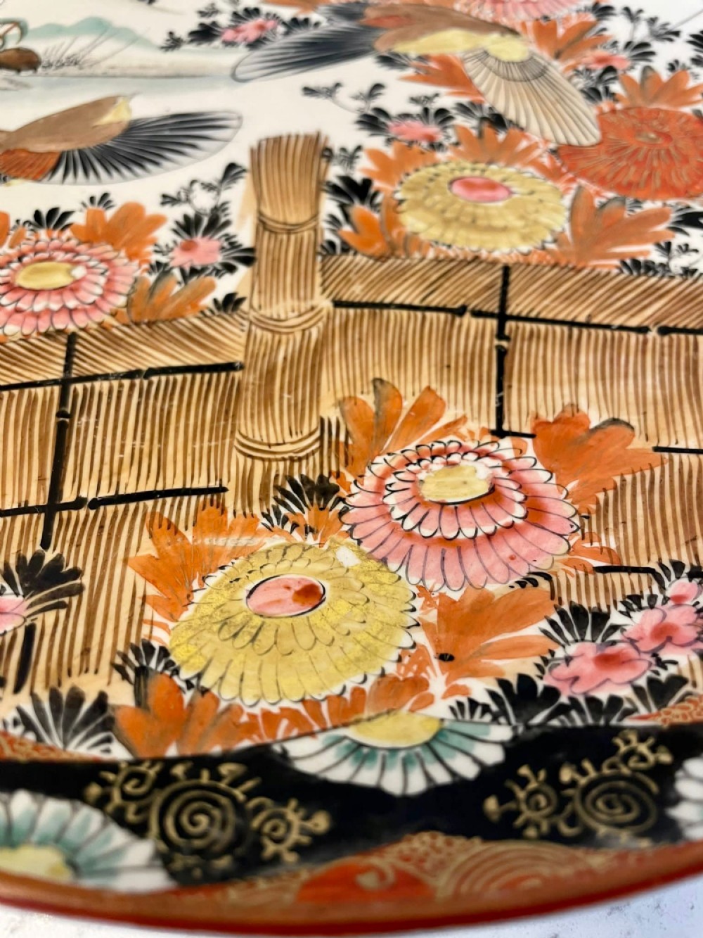 A shallow circular Japanese Kutani porcelain bowl featuring hand-painted floral chrysanthemum patterns, birds in flight, and detailed decorative borders in terracotta, red, black, and gold. View II
