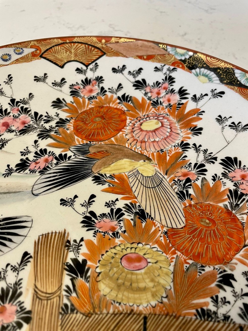 A shallow circular Japanese Kutani porcelain bowl featuring hand-painted floral chrysanthemum patterns, birds in flight, and detailed decorative borders in terracotta, red, black, and gold. View III