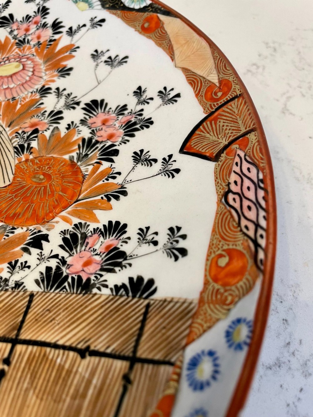 A shallow circular Japanese Kutani porcelain bowl featuring hand-painted floral chrysanthemum patterns, birds in flight, and detailed decorative borders in terracotta, red, black, and gold. View VI