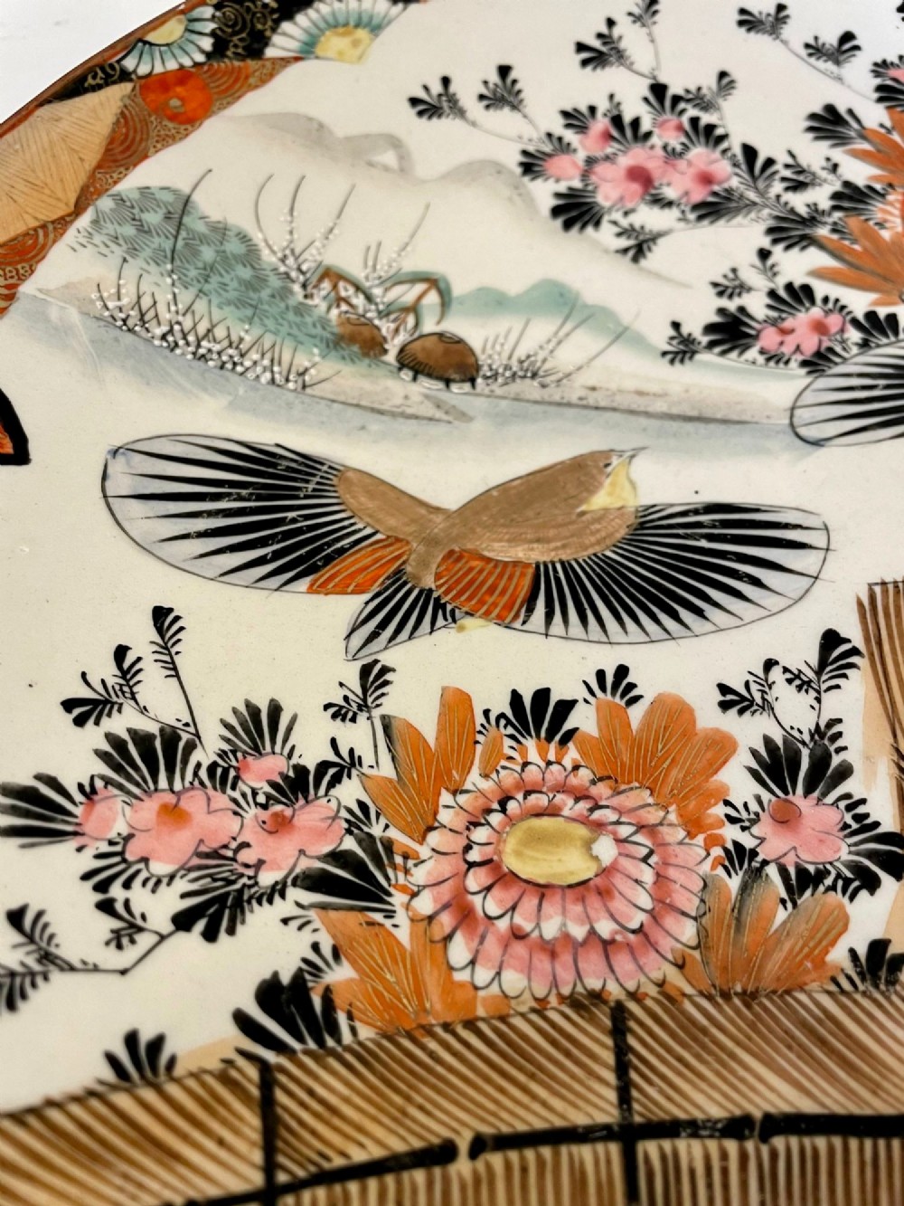 A shallow circular Japanese Kutani porcelain bowl featuring hand-painted floral chrysanthemum patterns, birds in flight, and detailed decorative borders in terracotta, red, black, and gold. View VIII