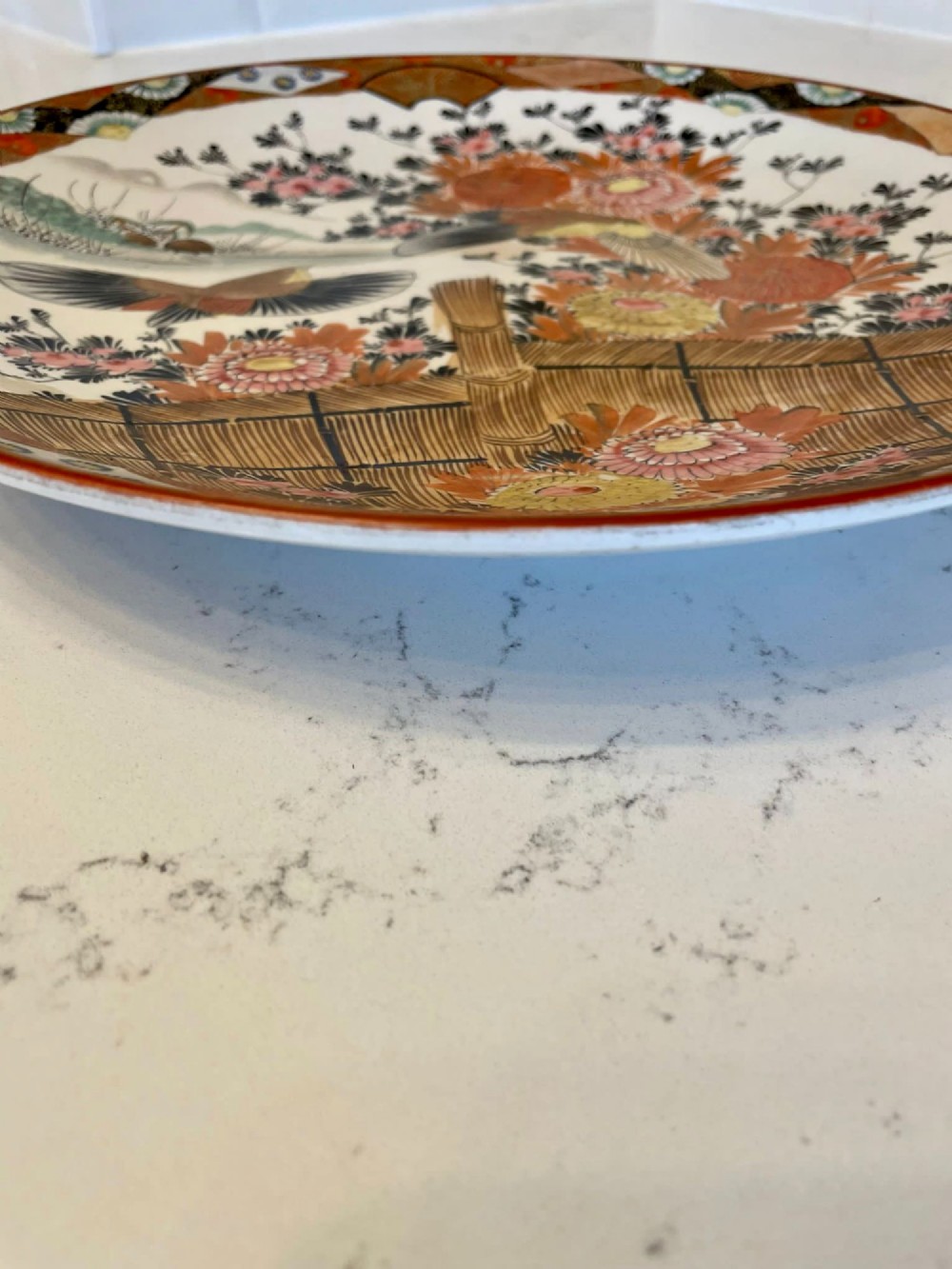 A shallow circular Japanese Kutani porcelain bowl featuring hand-painted floral chrysanthemum patterns, birds in flight, and detailed decorative borders in terracotta, red, black, and gold. View X