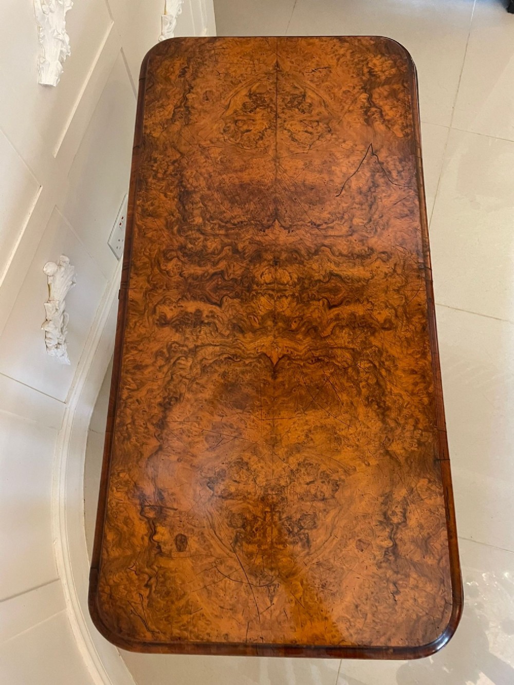 A Victorian burr walnut fold-over card table featuring a rectangular figured veneer top with rounded corners, twin turned pedestals, and carved legs on castors. View III
