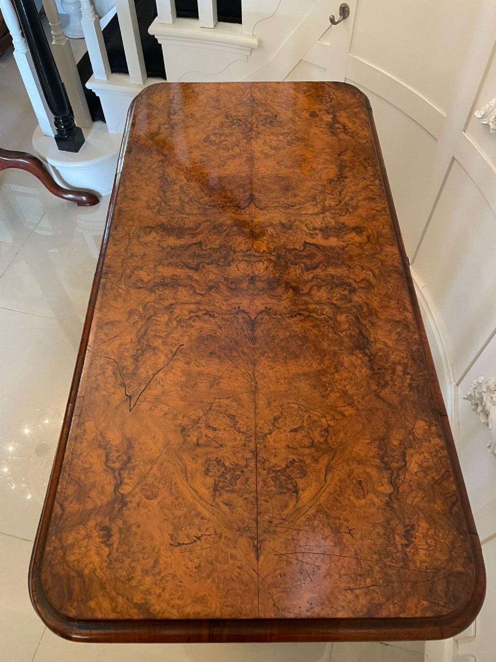 A Victorian burr walnut fold-over card table featuring a rectangular figured veneer top with rounded corners, twin turned pedestals, and carved legs on castors. View IV