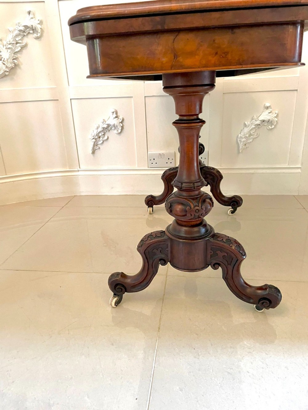 A Victorian burr walnut fold-over card table featuring a rectangular figured veneer top with rounded corners, twin turned pedestals, and carved legs on castors. View VI