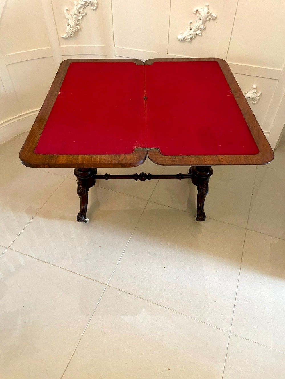 A Victorian burr walnut fold-over card table featuring a rectangular figured veneer top with rounded corners, twin turned pedestals, and carved legs on castors. View X