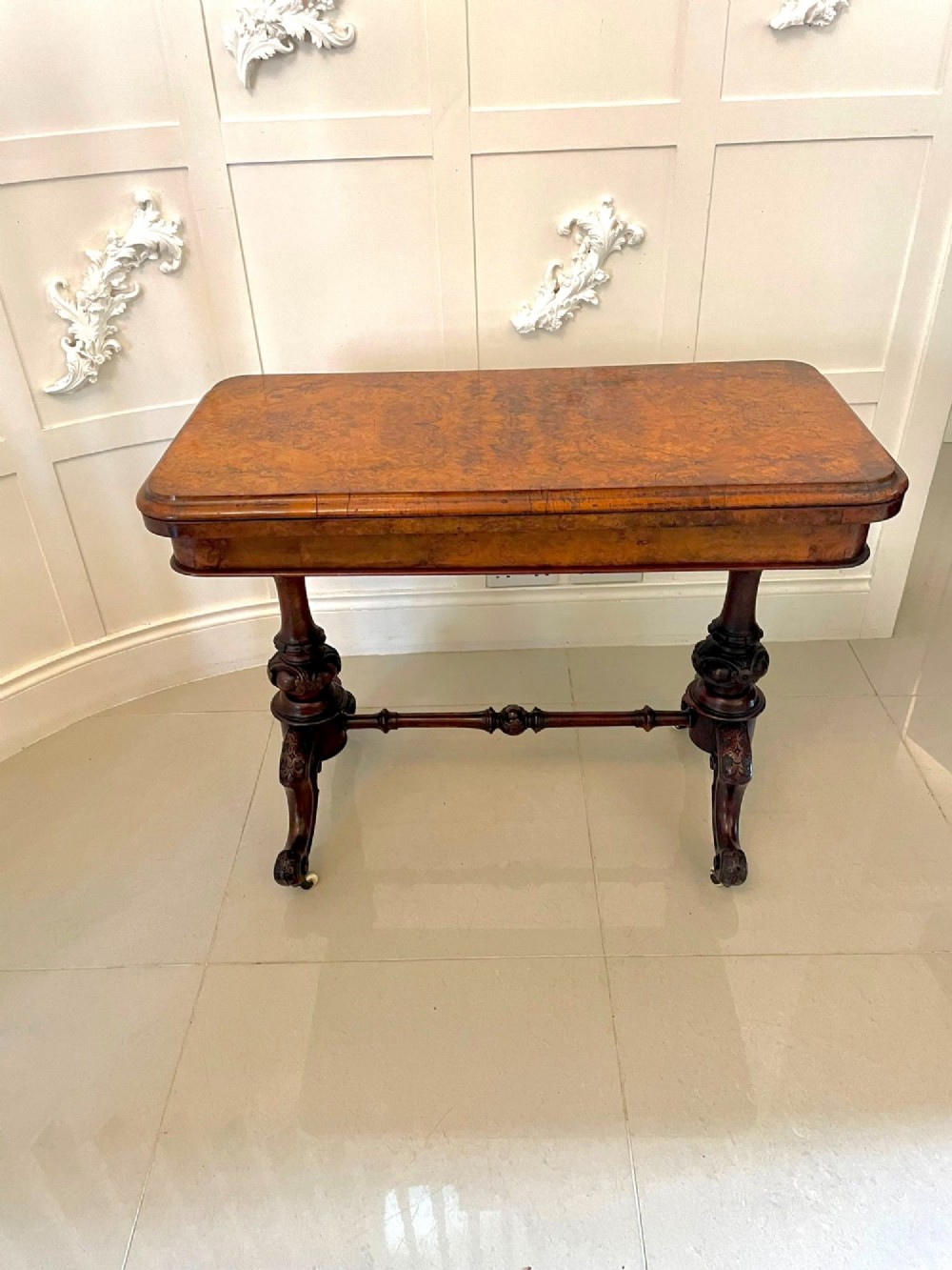 A Victorian burr walnut fold-over card table featuring a rectangular figured veneer top with rounded corners, twin turned pedestals, and carved legs on castors. View XIII