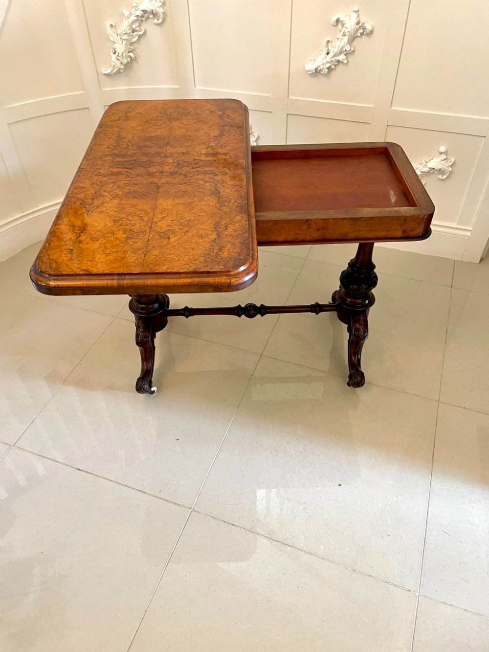 A Victorian burr walnut fold-over card table featuring a rectangular figured veneer top with rounded corners, twin turned pedestals, and carved legs on castors. View XV