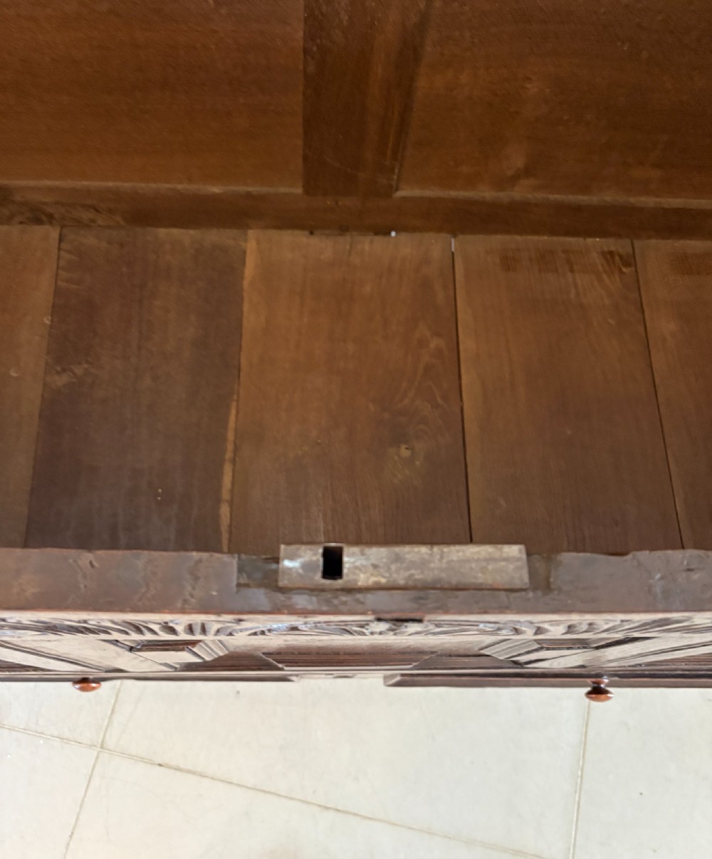 A 17th-century dark oak mule chest featuring a hinged paneled lid, a carved frieze above geometric front panels, and two lower drawers with wooden knobs. View V