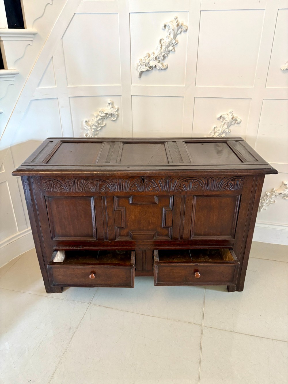 A 17th-century dark oak mule chest featuring a hinged paneled lid, a carved frieze above geometric front panels, and two lower drawers with wooden knobs. View VIII