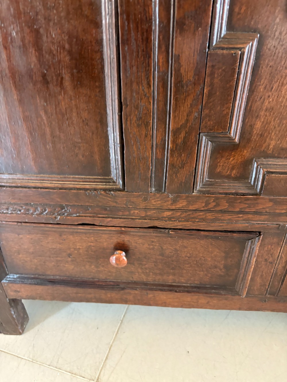A 17th-century dark oak mule chest featuring a hinged paneled lid, a carved frieze above geometric front panels, and two lower drawers with wooden knobs. View X
