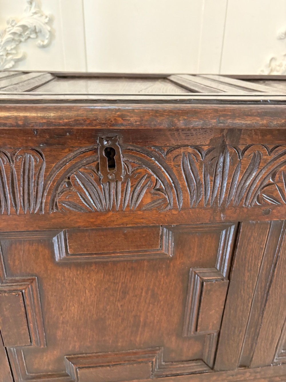 A 17th-century dark oak mule chest featuring a hinged paneled lid, a carved frieze above geometric front panels, and two lower drawers with wooden knobs. View XI