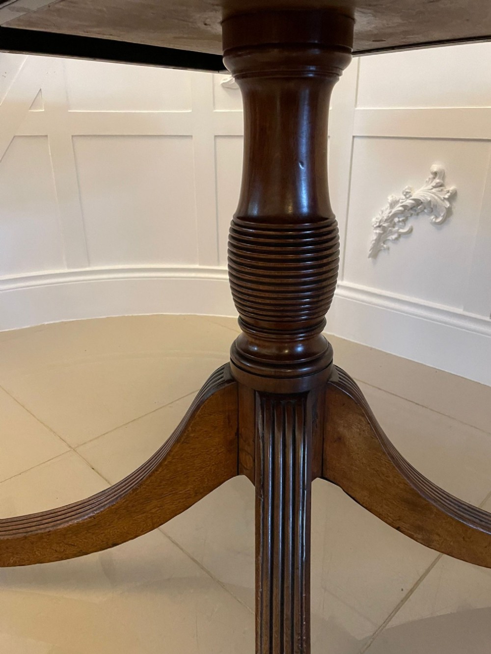An antique George III oval tilt-top dining table in flame mahogany, featuring a crossbanded border and a quadruped pedestal base with reeded legs and brass castors. View IX