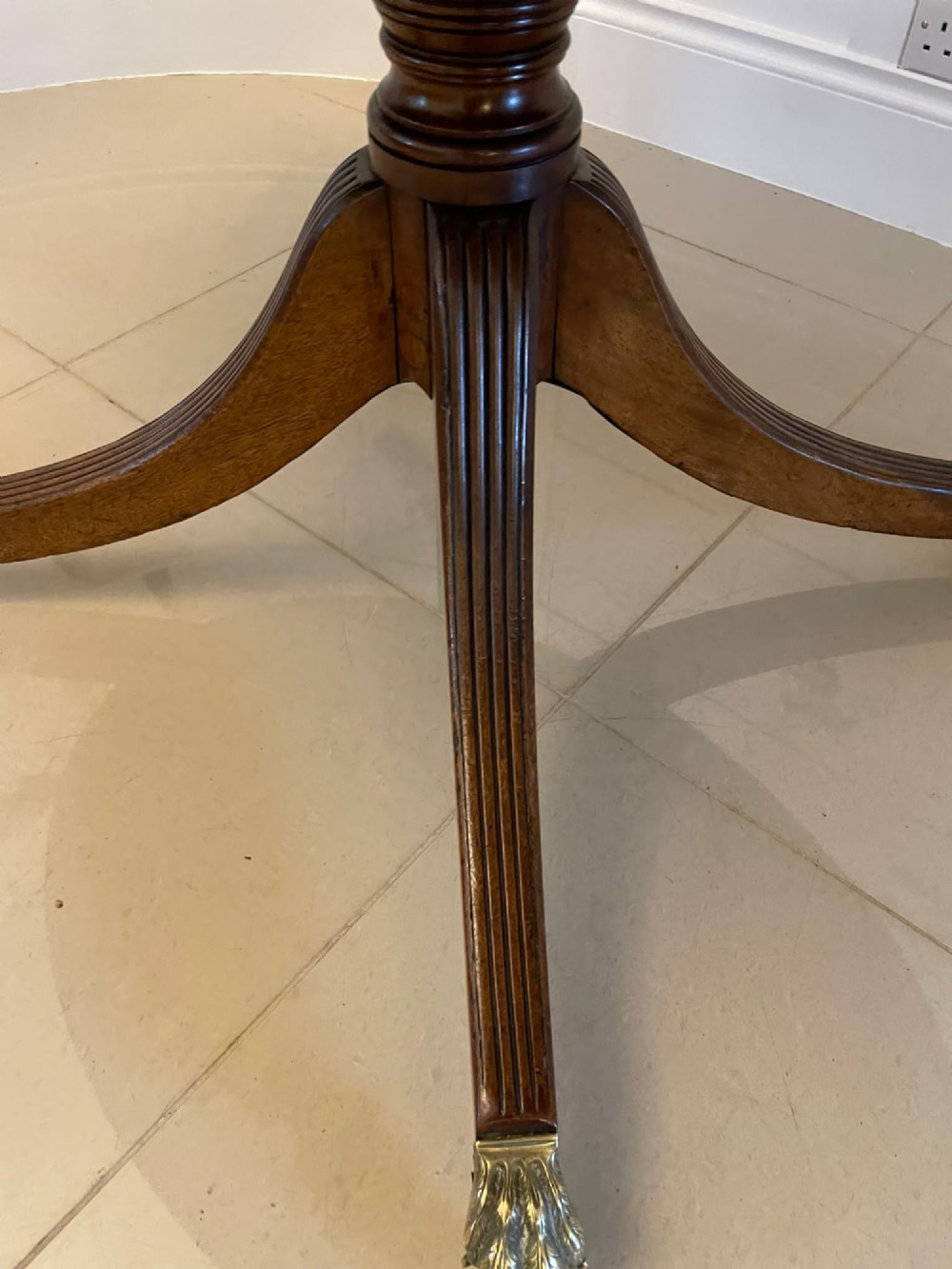 An antique George III oval tilt-top dining table in flame mahogany, featuring a crossbanded border and a quadruped pedestal base with reeded legs and brass castors. View XI