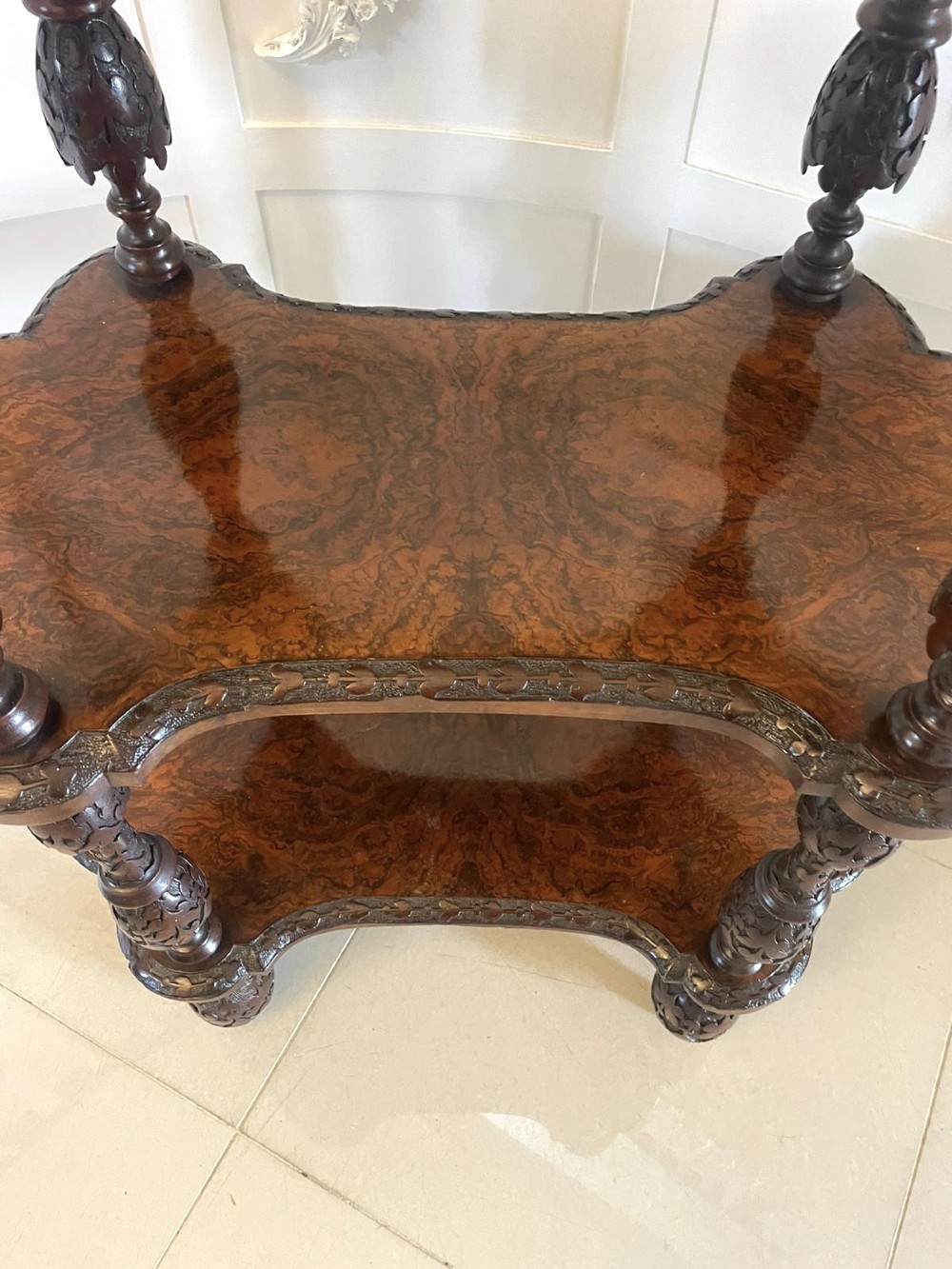 A Victorian burr walnut three-tier whatnot with intricately carved foliage uprights, finials, and serpentine-shaped shelves. View V