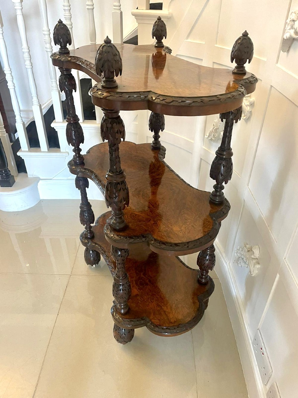 A Victorian burr walnut three-tier whatnot with intricately carved foliage uprights, finials, and serpentine-shaped shelves. View VI