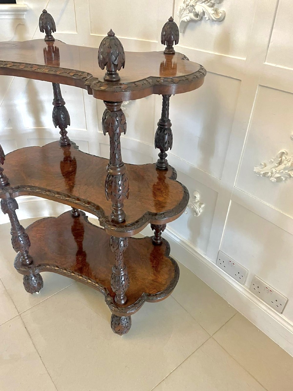 A Victorian burr walnut three-tier whatnot with intricately carved foliage uprights, finials, and serpentine-shaped shelves. View VII