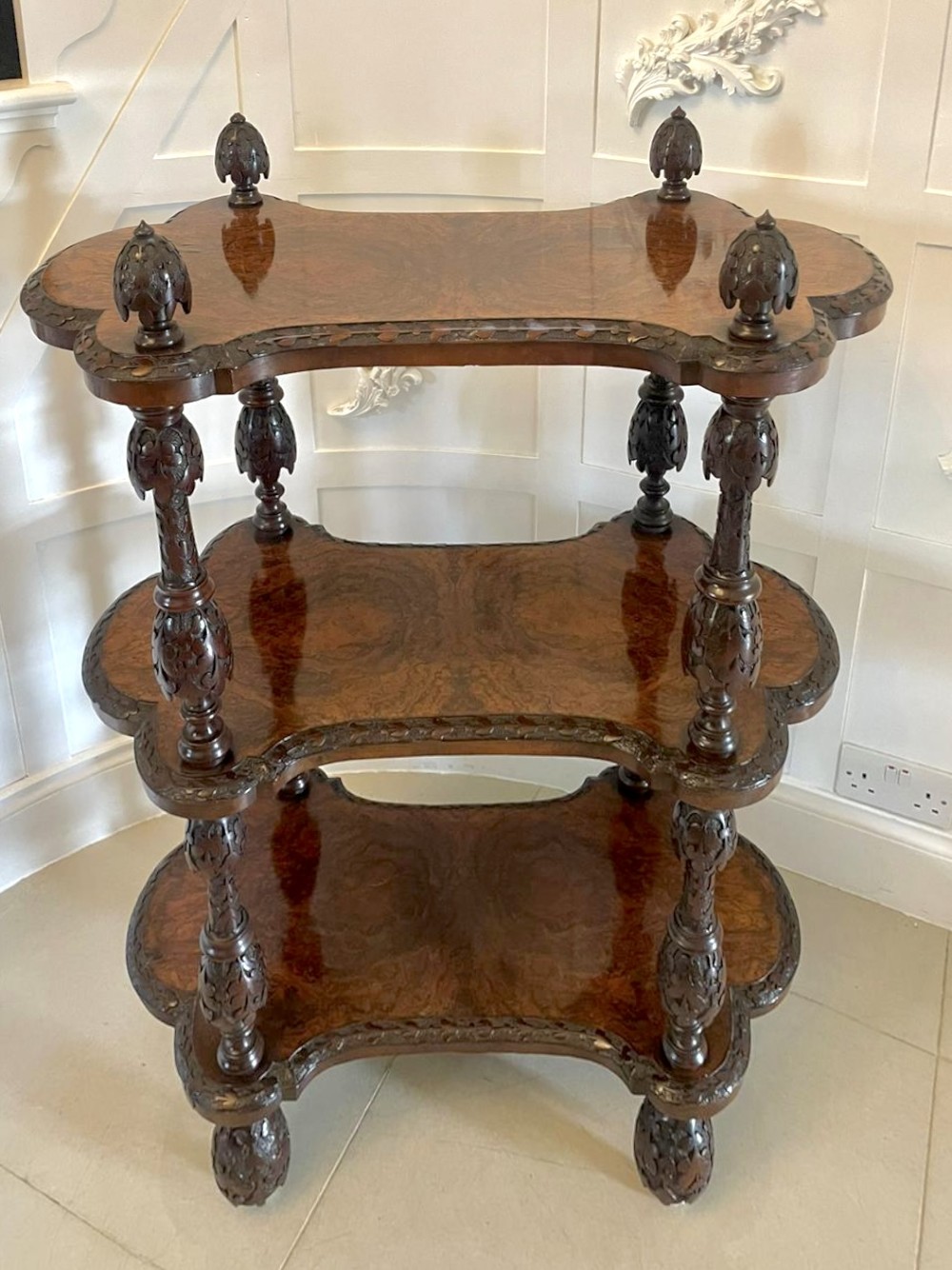 A Victorian burr walnut three-tier whatnot with intricately carved foliage uprights, finials, and serpentine-shaped shelves. View XII