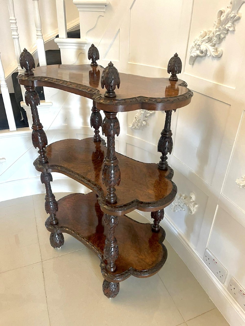 A Victorian burr walnut three-tier whatnot with intricately carved foliage uprights, finials, and serpentine-shaped shelves. View XIV