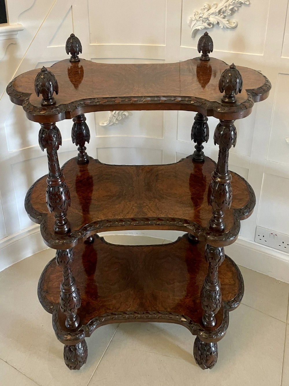 A Victorian burr walnut three-tier whatnot with intricately carved foliage uprights, finials, and serpentine-shaped shelves. View XV