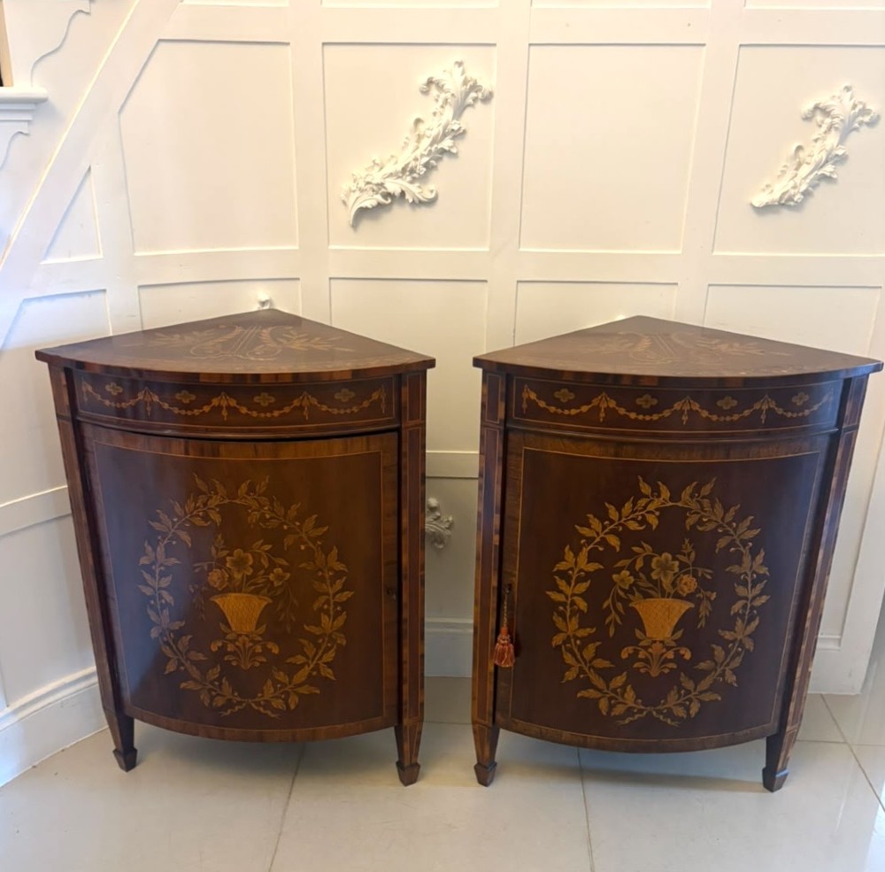 A pair of Victorian mahogany corner cabinets featuring curved bow fronts with floral urn marquetry inlays and tapered square feet.