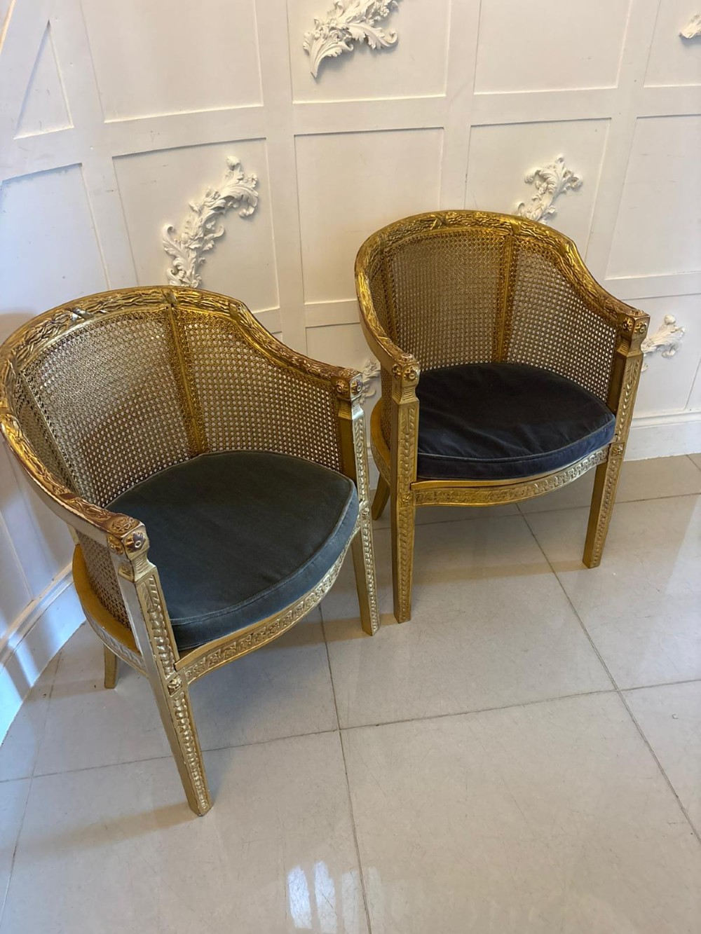 A pair of French Louis XVI style carved giltwood tub armchairs featuring curved caned backs and dark blue velvet seat cushions. View V
