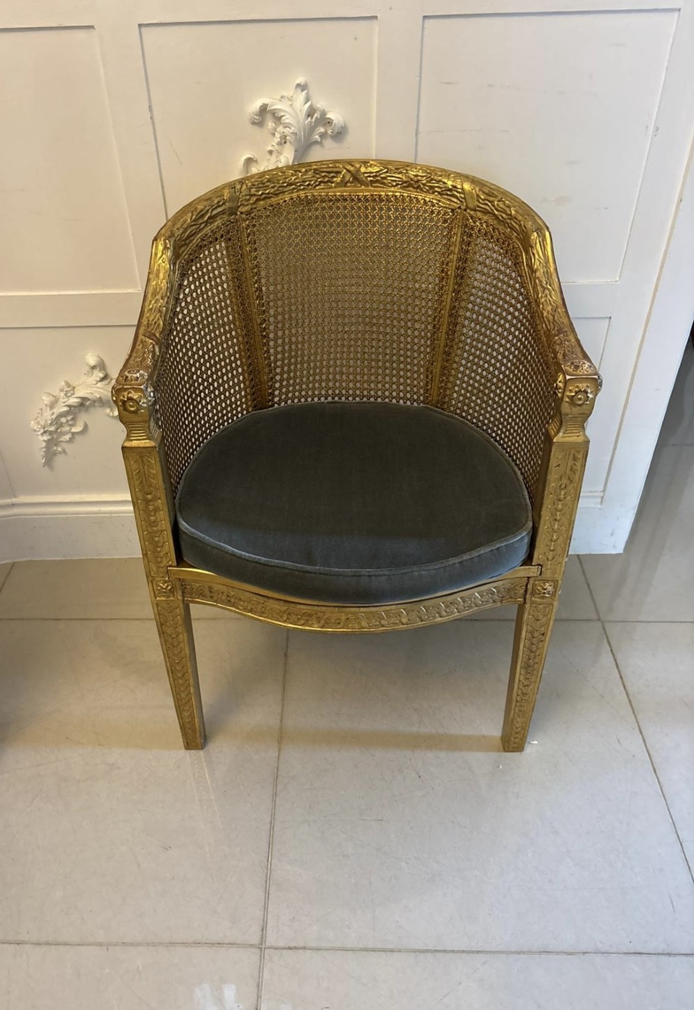 A pair of French Louis XVI style carved giltwood tub armchairs featuring curved caned backs and dark blue velvet seat cushions. View VII