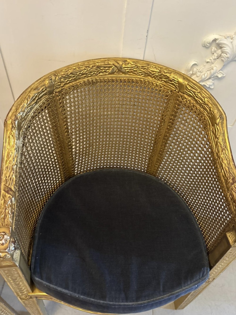 A pair of French Louis XVI style carved giltwood tub armchairs featuring curved caned backs and dark blue velvet seat cushions. View VIII